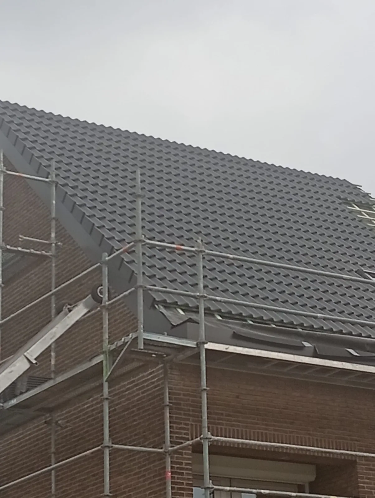 Nieuwe donkere dakpannen op een hellend dak met stelling
